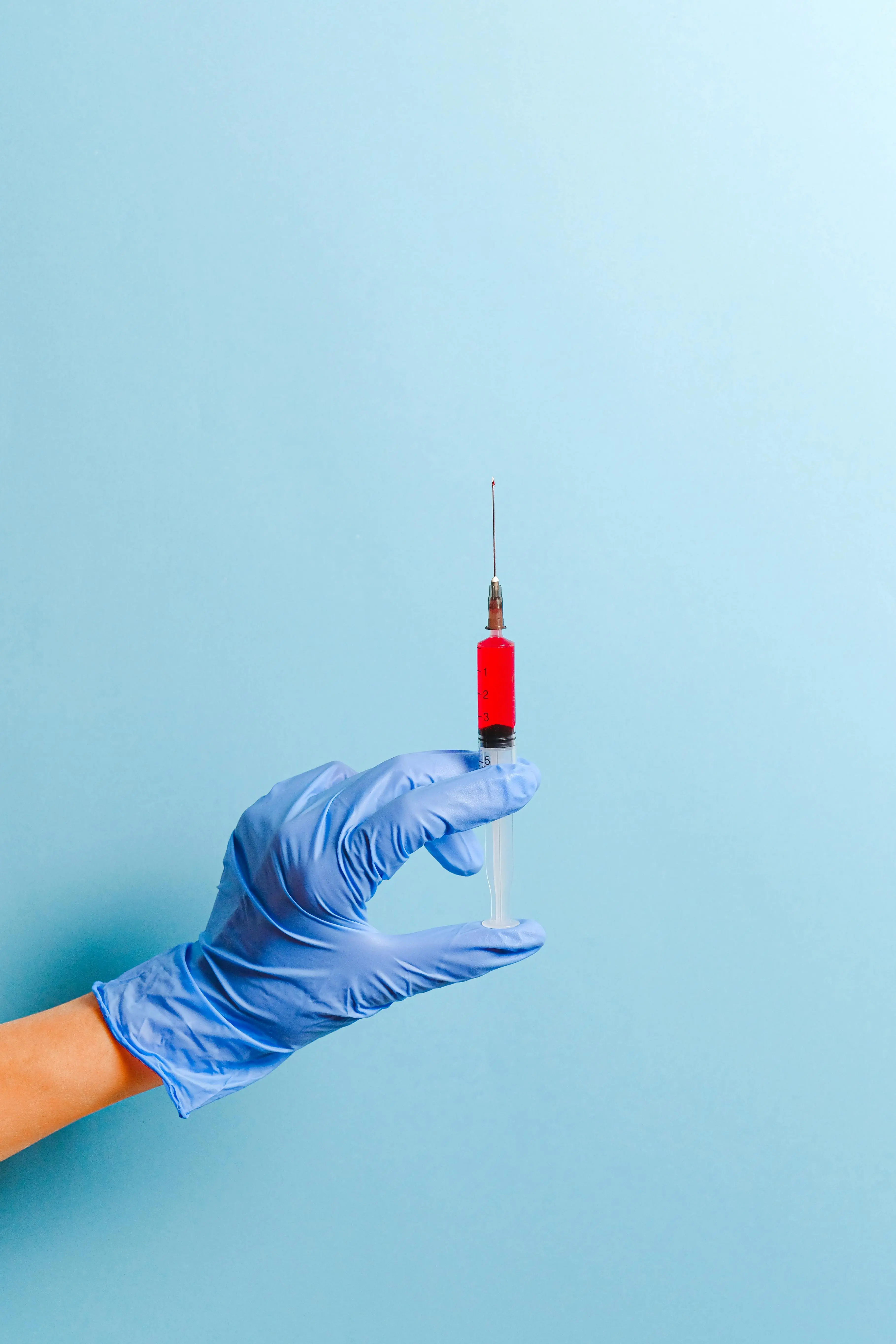 Hand mit blauem Handschuh und Spritze mit roter Flüssigkeit