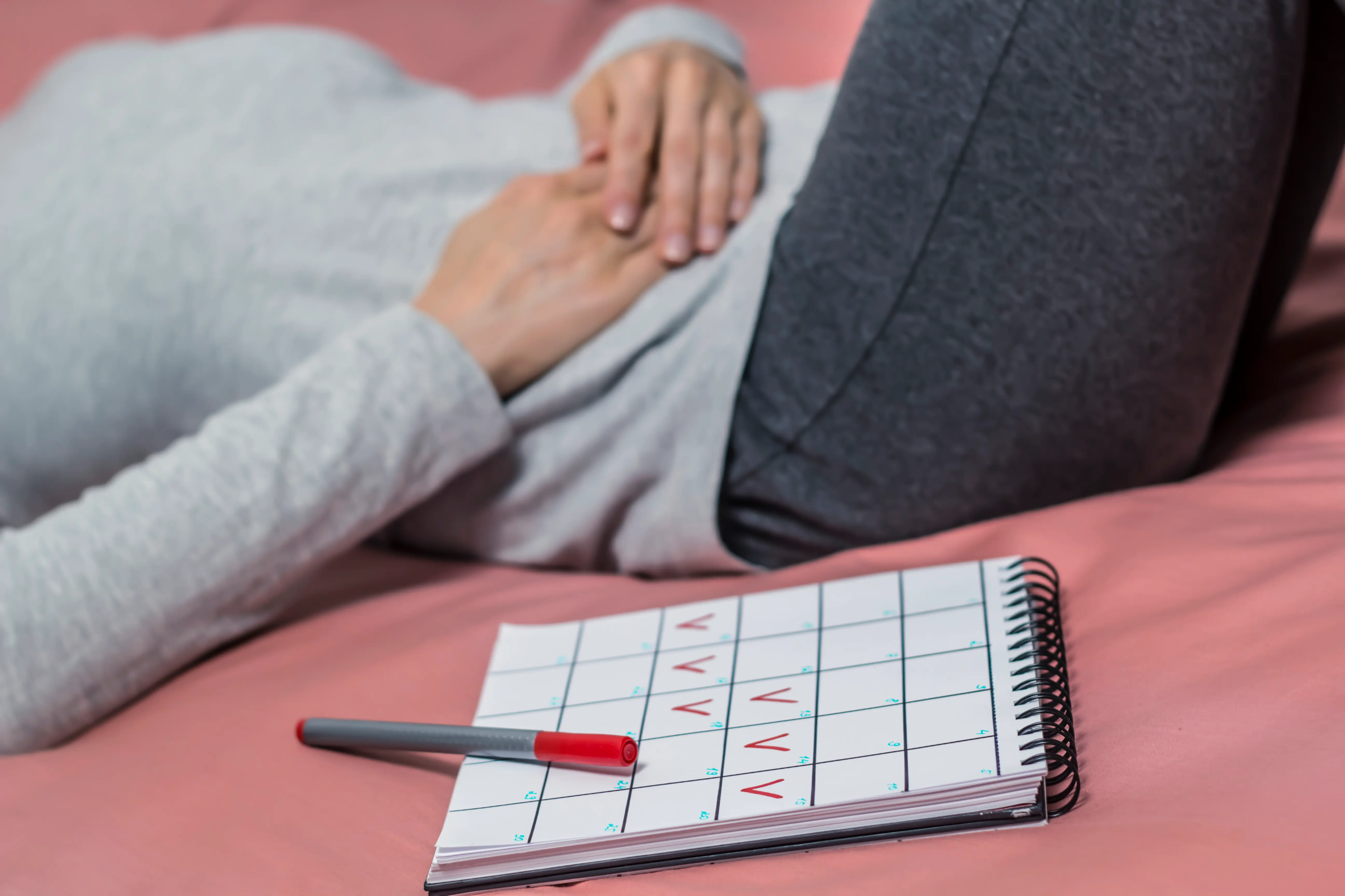 Frau hält sich Bauch, Schmerzen, Menstruationskalender